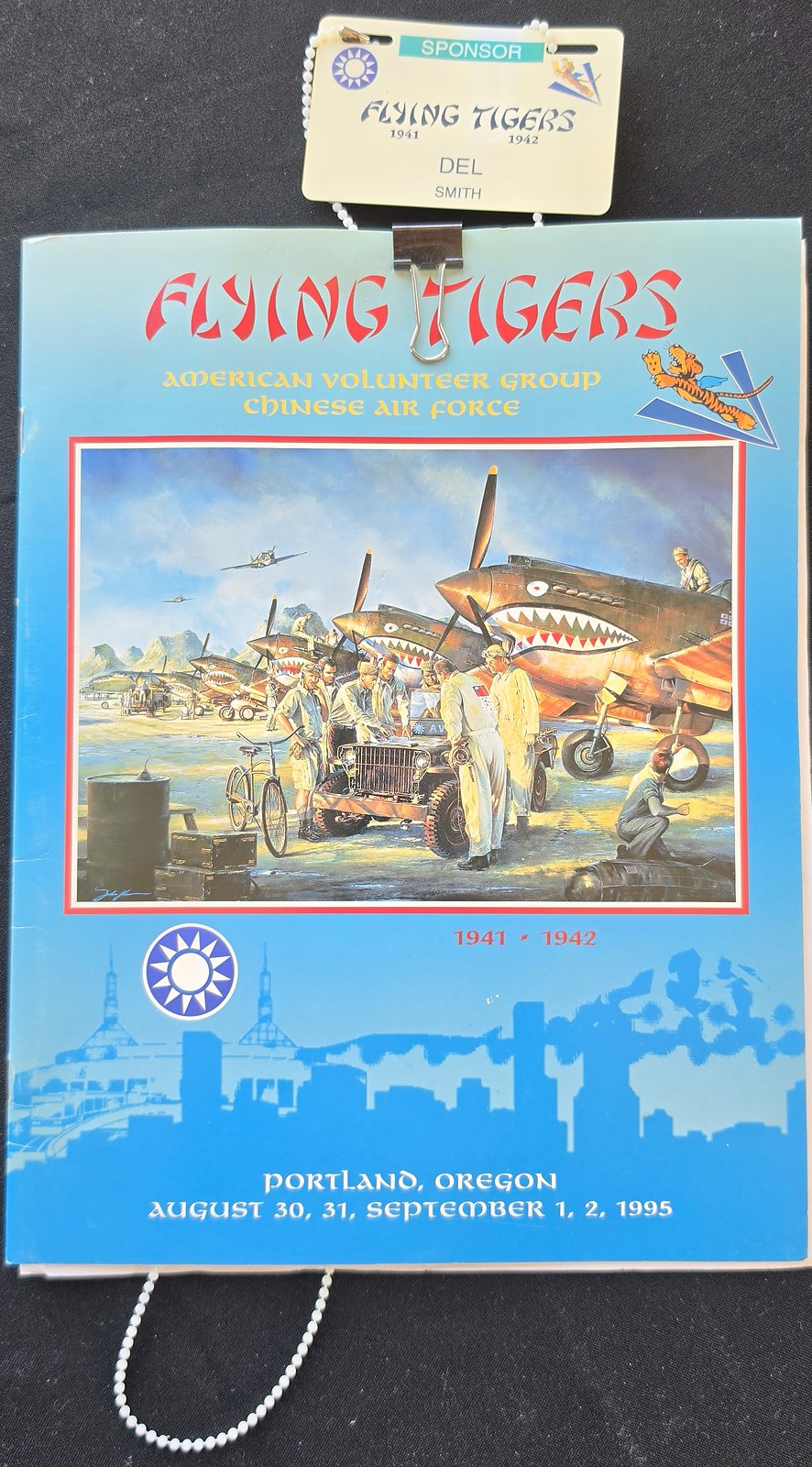 Program cover for Flying Tigers, American Volunteer Group, Chinese Air Force, 1941 to 1942, Portland, Oregon, August 30 to September 2, 1995, with a painting of shark-mouth P-40 fighters, and a name badge reading Sponsor, Del Smith clipped to the top